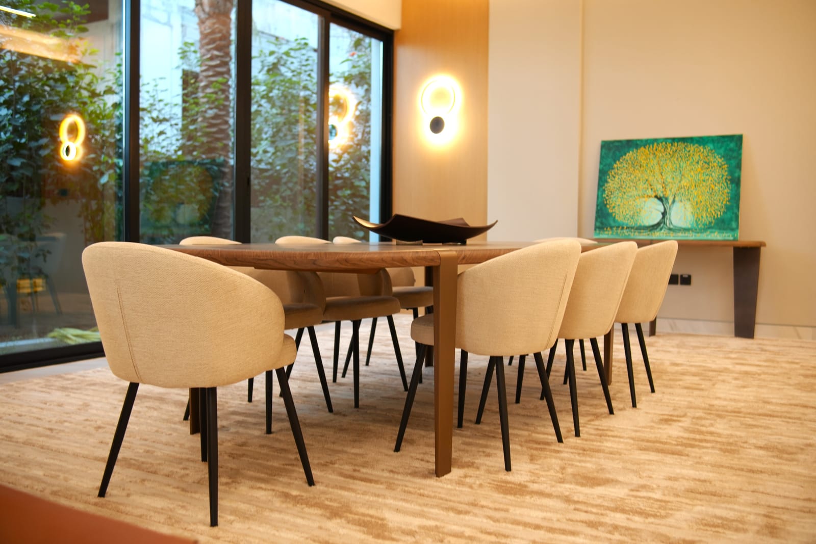 Dining room with a solid timber table, boucle chairs and wall sconces beside floor-to-ceiling glazing