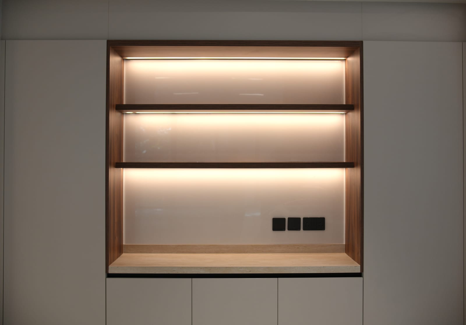 Backlit walnut display niche with floating shelves and a travertine base