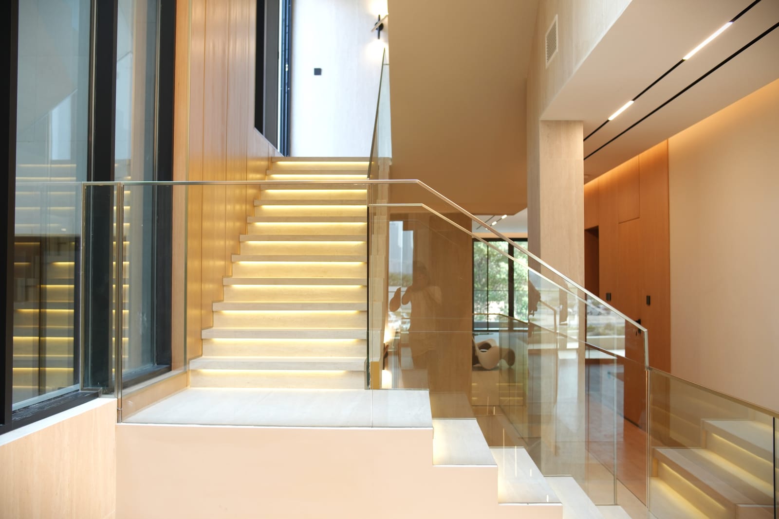 Double-height stair hall with a travertine staircase, glass balustrade and warm timber walls in a Meydan villa