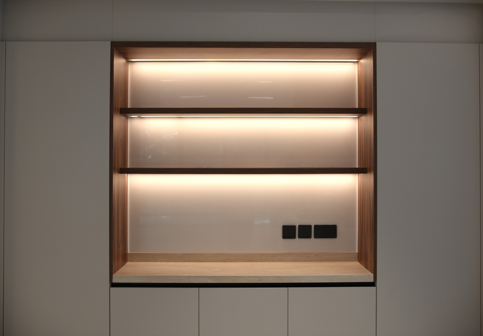 Backlit walnut display niche with travertine base and bespoke joinery